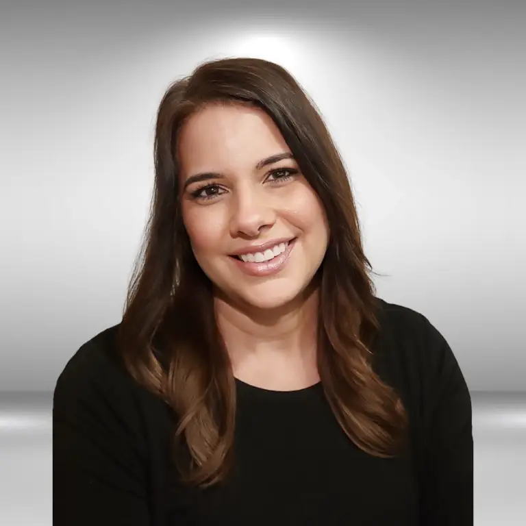 A woman with long brown hair is smiling, wearing a black top, and posing against a gray gradient background, capturing the essence of an influencer's polished look.