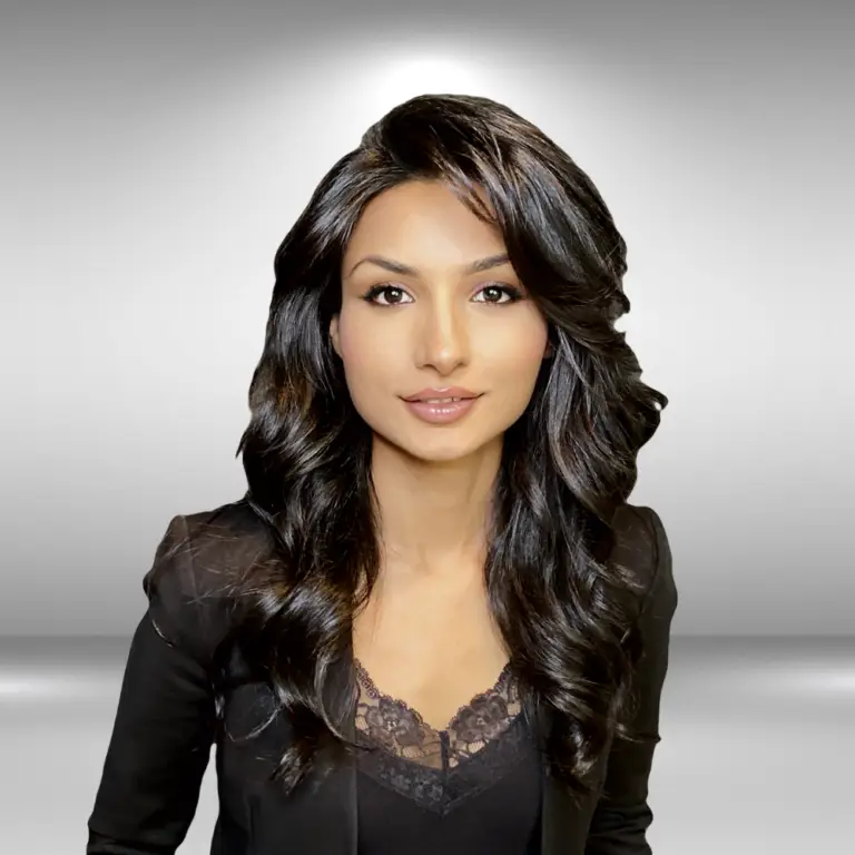 A woman with long, wavy black hair is wearing a dark blazer over a lacy top. She stands against a neutral gradient background and looks directly at the camera with a slight smile, exuding the confidence of an influencer ready for her next audition.