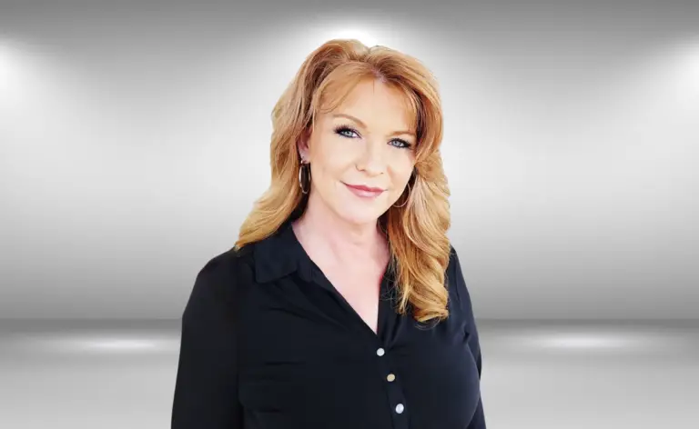 A woman with long, wavy, light brown hair wearing hoop earrings and a black blouse stands in front of a plain gray background. She has a slight smile and is looking directly at the camera, exuding an air of confidence as if ready for a runway audition. The background features subtle lighting and gradients.