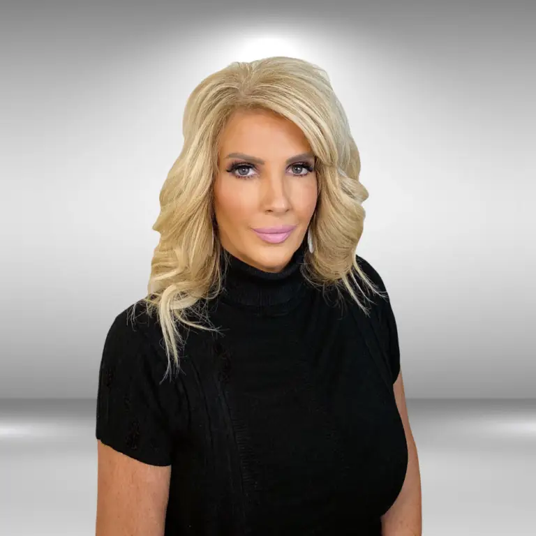 A model with long, wavy blonde hair is wearing a black turtleneck top. She has a neutral expression and is posed against a plain, light-gray background.