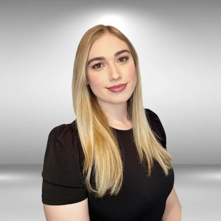 A young woman with long blonde hair stands against a bright, gradient background. She is wearing a black shirt and has a slight smile on her face. Her expression is calm, and her gaze is directed towards the camera, as if she is ready for an important audition.