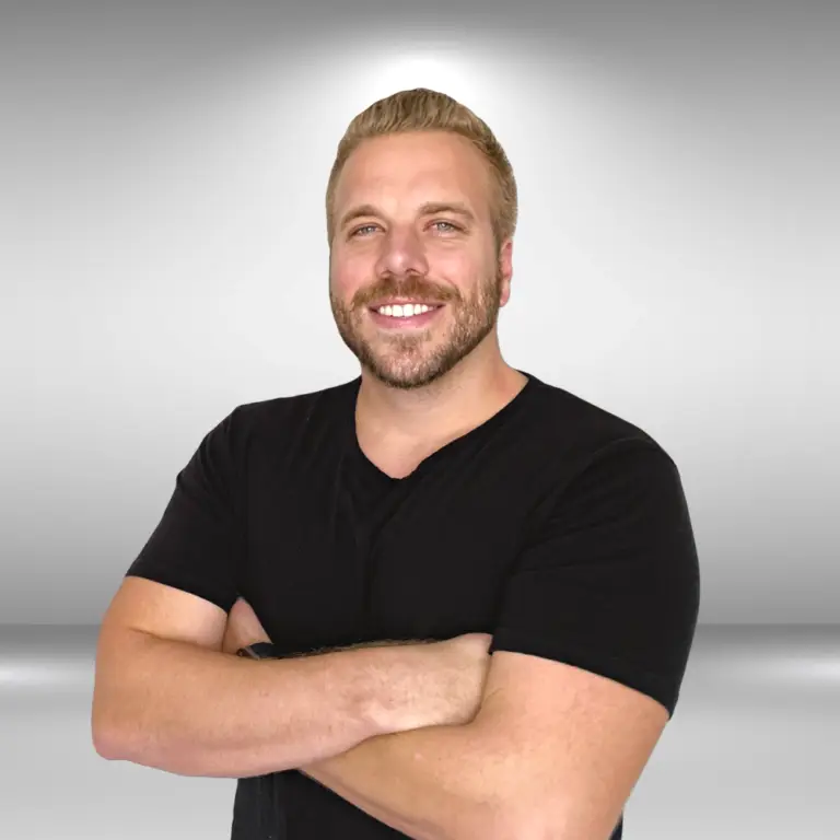 A man with light hair and a beard is standing with his arms crossed, smiling at the camera. He exudes talent, wearing a black t-shirt against a simple, light-colored gradient background, ready for his audition.