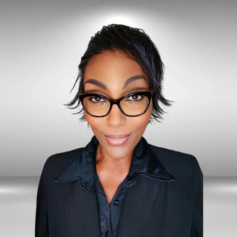 A person with short black hair and stylish black-framed glasses is wearing a black collared shirt and jacket. The background is a gradient of light to dark gray, adding a professional ambiance to the portrait, reminiscent of an actor's poised elegance or an influencer's polished style.