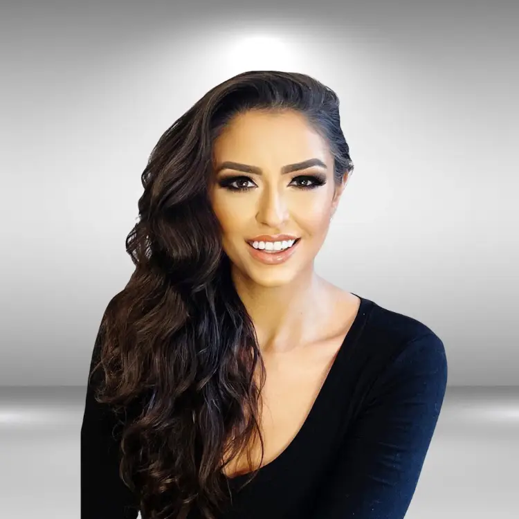 A woman with long, wavy, dark hair is smiling in front of a light grey background. She is wearing a fitted black top with a V-neckline and has a confident expression, embodying the poise of an influencer.