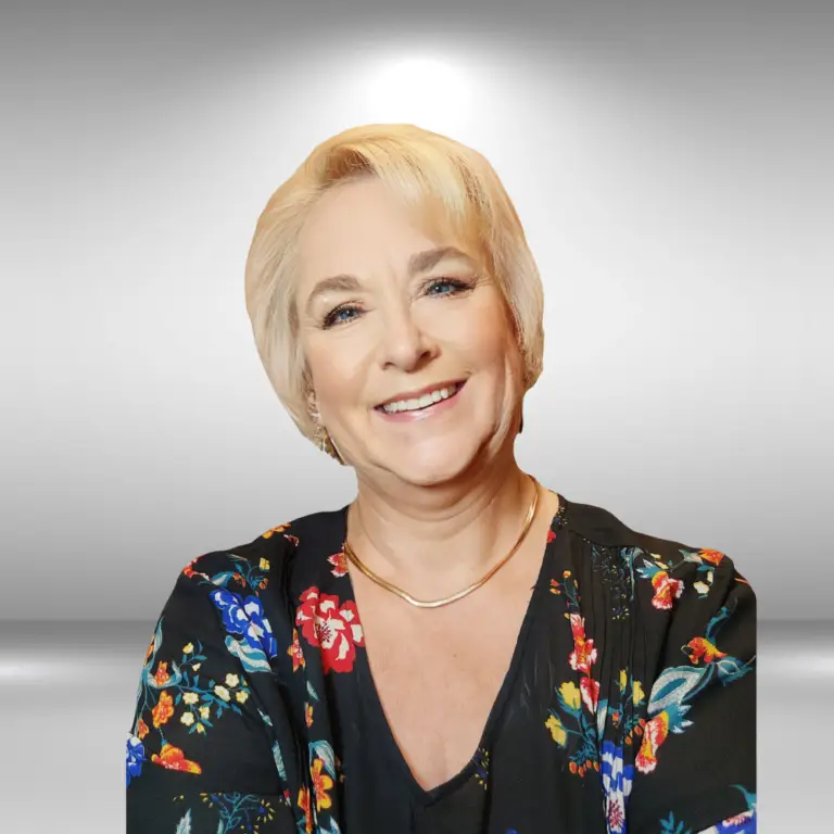 A smiling woman with short blonde hair, wearing a black floral top and a gold necklace, stands ready for her audition. The background is a gradient of gray, fading to white behind her head, creating a halo effect that highlights her talent.