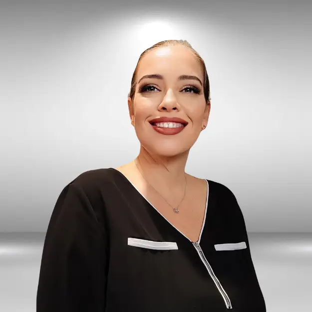 A talented individual with slicked-back hair, dark eyeliner, and a smile, wearing a black top with a zippered front and white accents. They are posed against a gradient gray background, exuding confidence like an influencer on the runway.