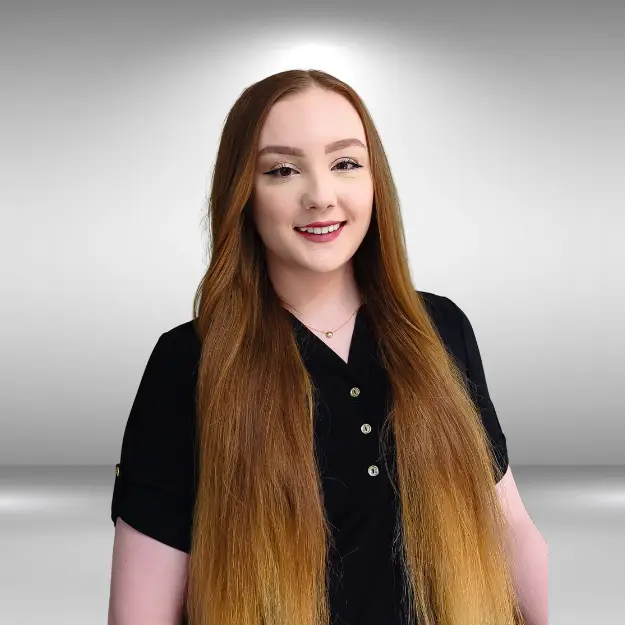 A person with long, straight, light brown hair is smiling while wearing a black shirt with buttons, as if ready for a runway. The background is a plain, gray gradient.