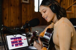 singer recording a song with guitar in hand in front of a laptop open to recording software