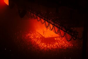 artist standing on a suspended stage in a stadium, with red light shining down