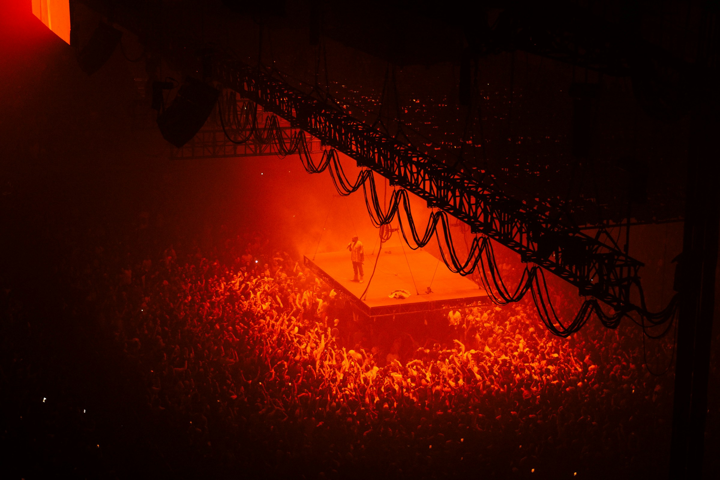 artist standing on a suspended stage in a stadium, with red light shining down